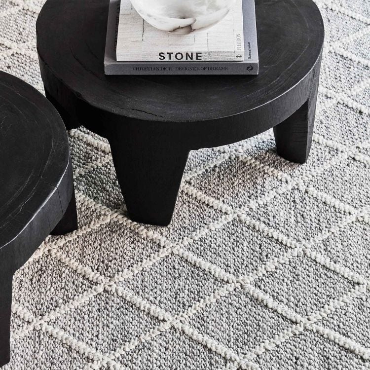 A blue grey rug with diamond shaped accents and a black wooden coffee table on top