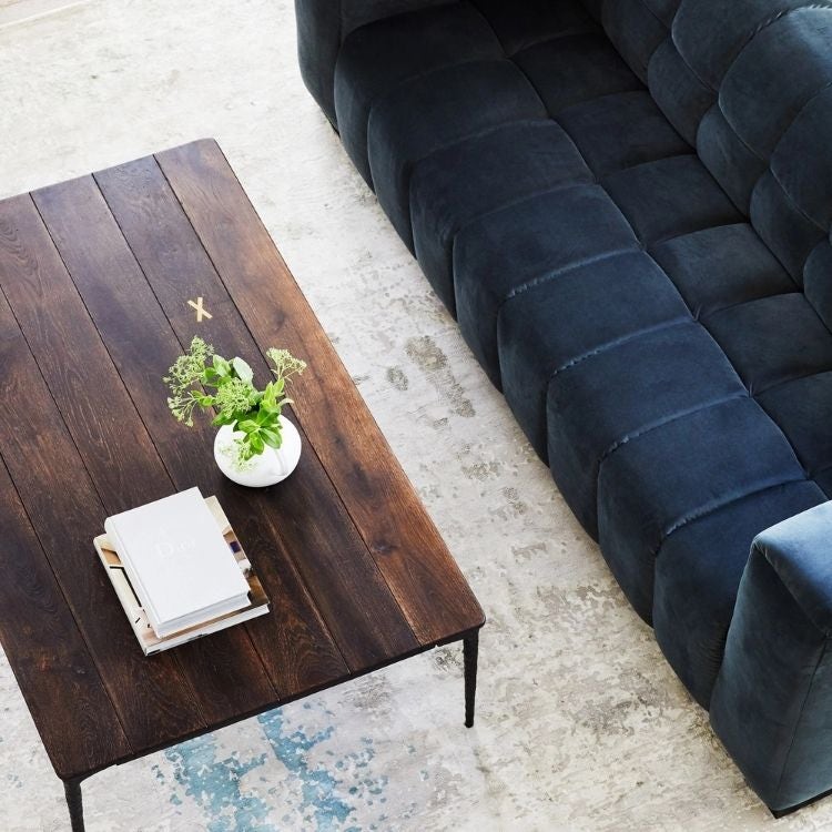 a beige and blue rug next to a blue sofa with a brown timber coffee table on top